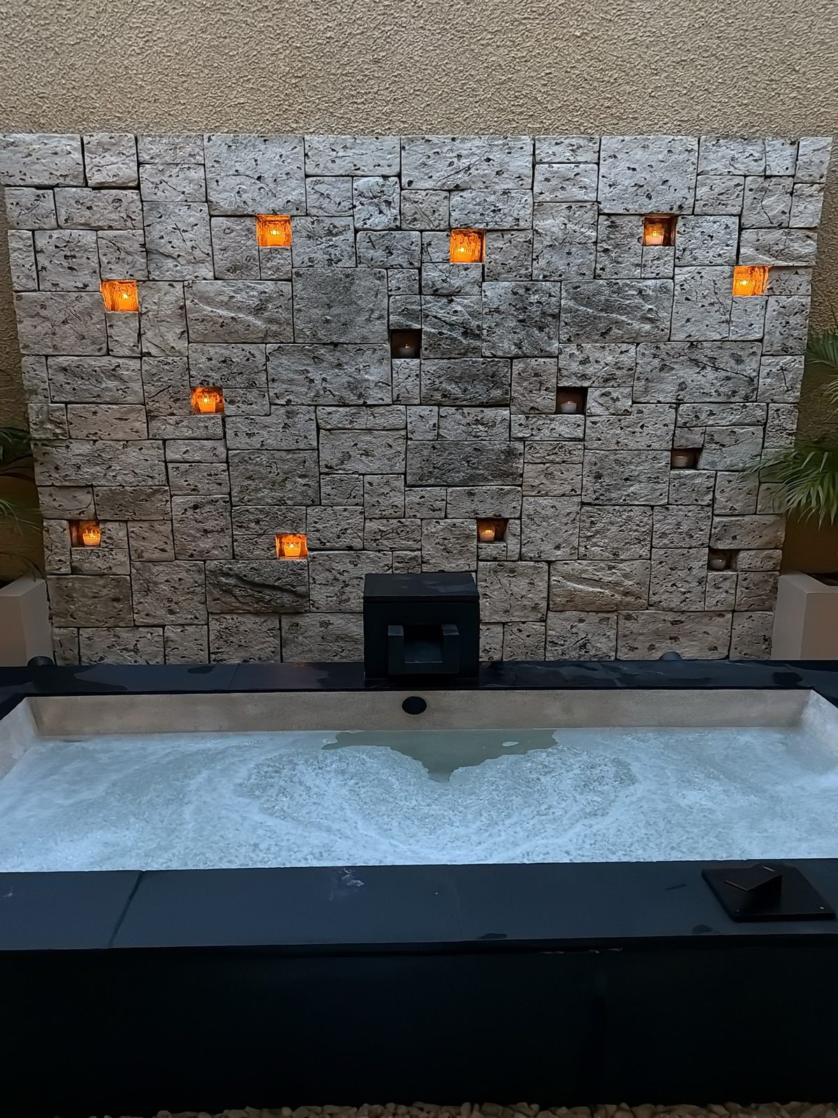 Outdoor bathtub filled and lit by tea lights set into a stone wall