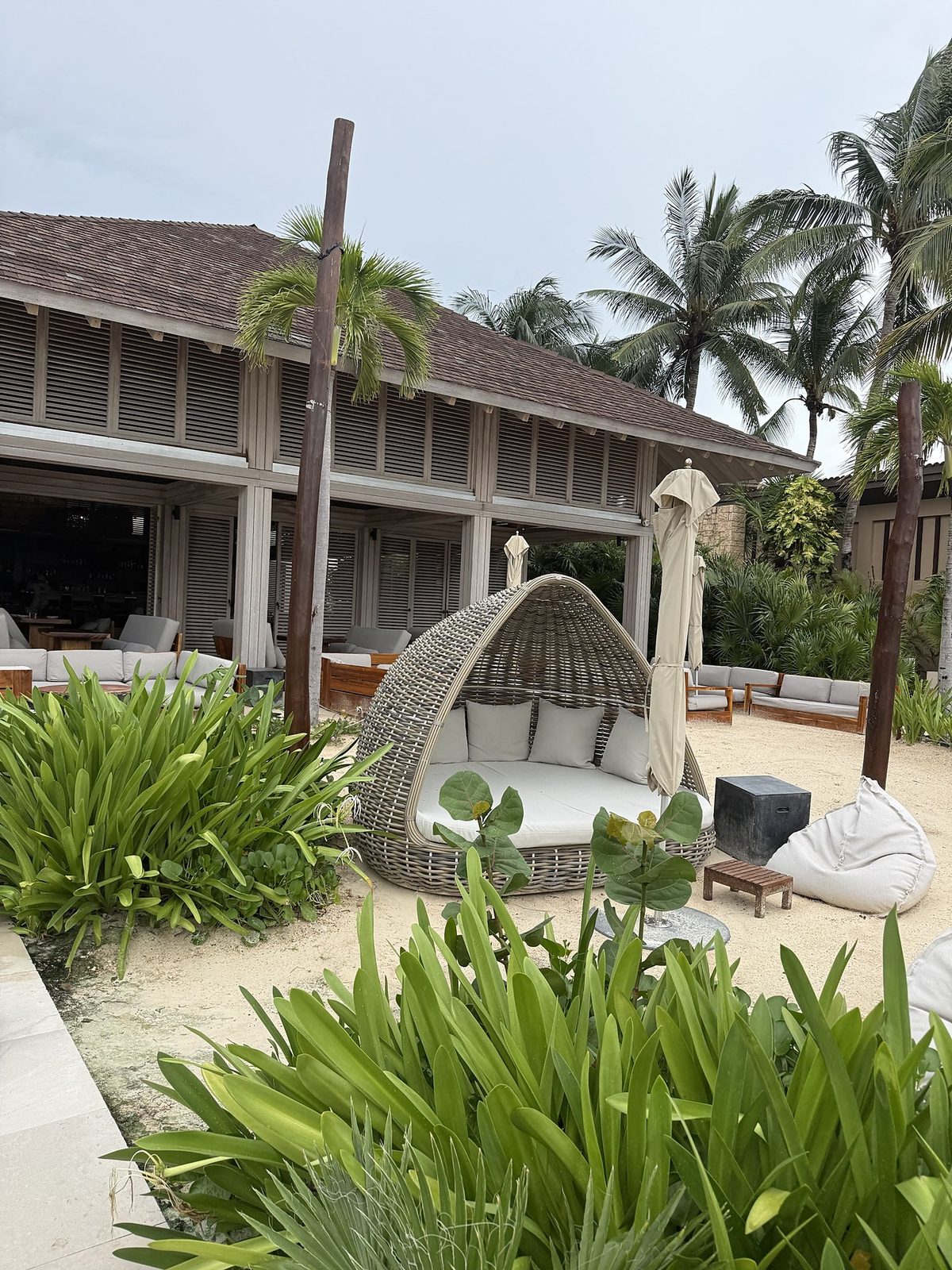 Woven rattan beach pod with cushions, under palms at Sands Beach Club