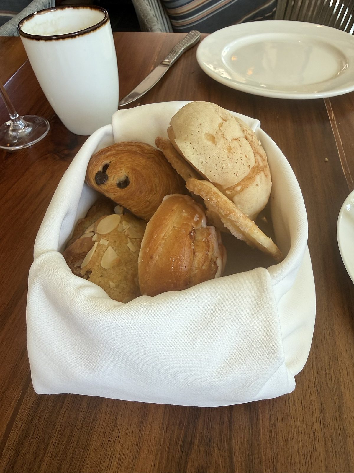 Bread basket with concha, pain au chocolat and almond pastry, beside a latte