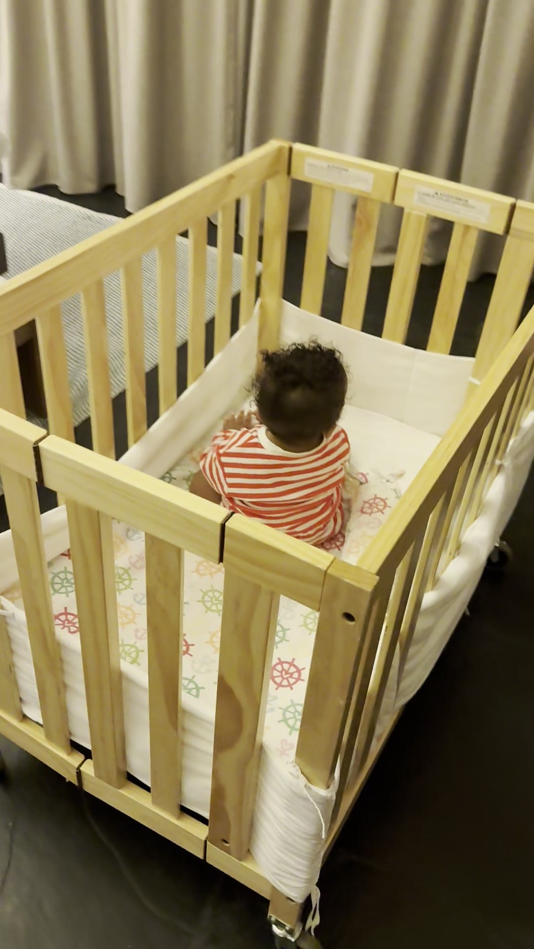 A full-size wooden crib on wheels with mesh sides and printed sheets, set up in the villa