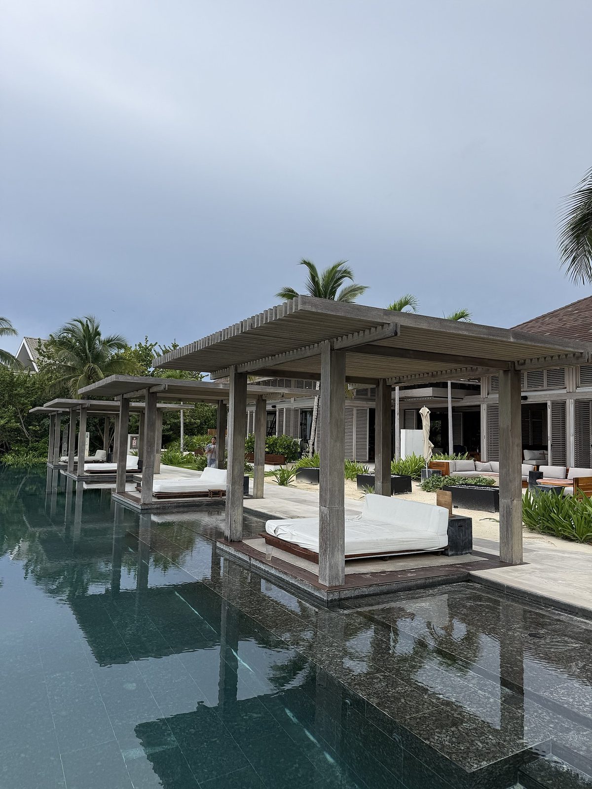 Shaded daybeds on platforms over water under timber pergolas at Sands Beach Club