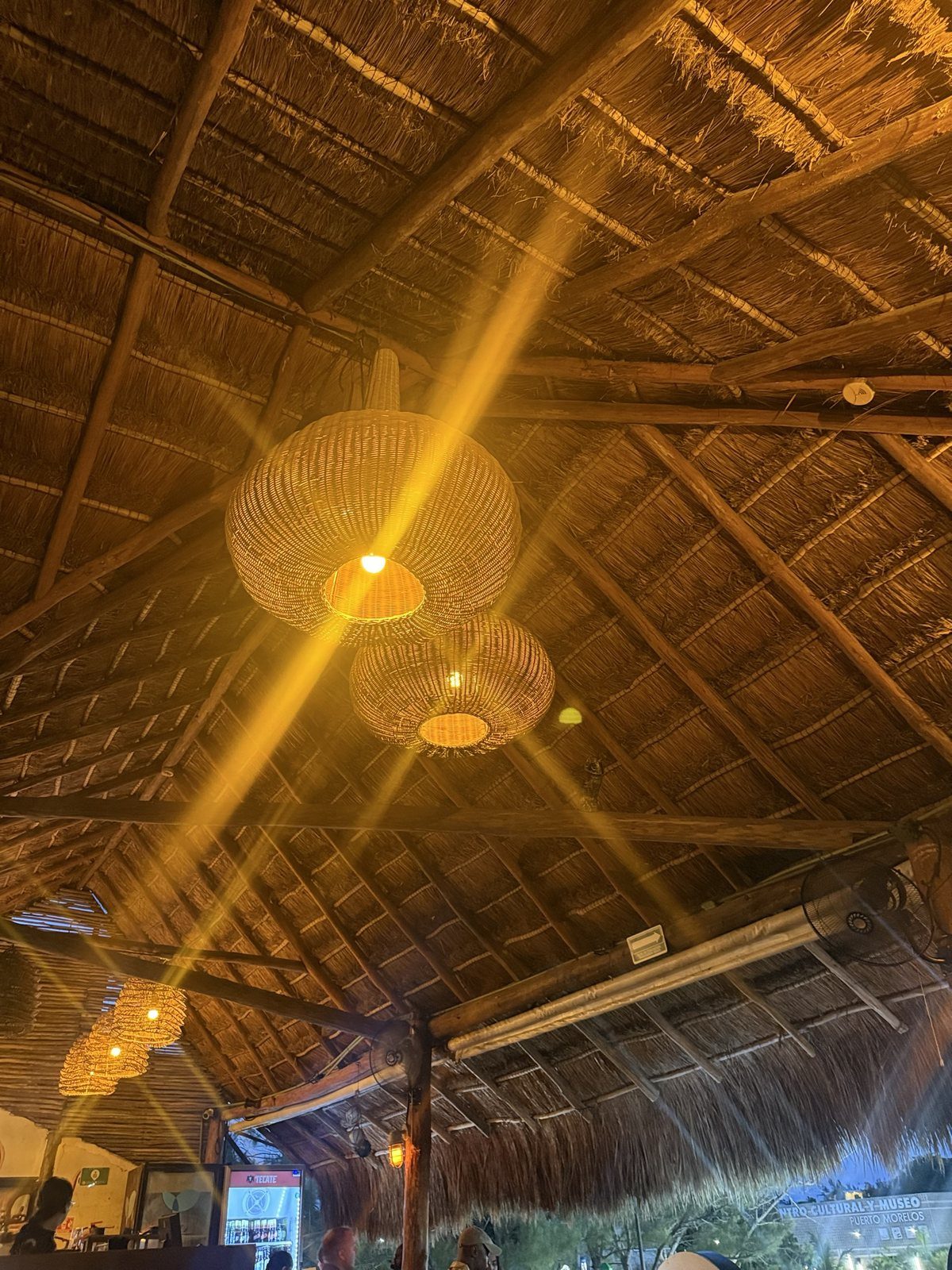 Large woven pendant lamps hanging from a thatched palapa roof above the dining room