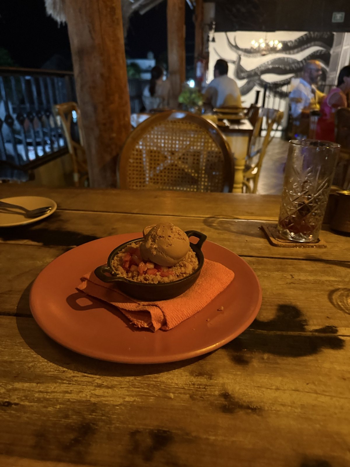 A strawberry crumble in a small cast-iron dish topped with salted caramel ice cream, on a terracotta plate