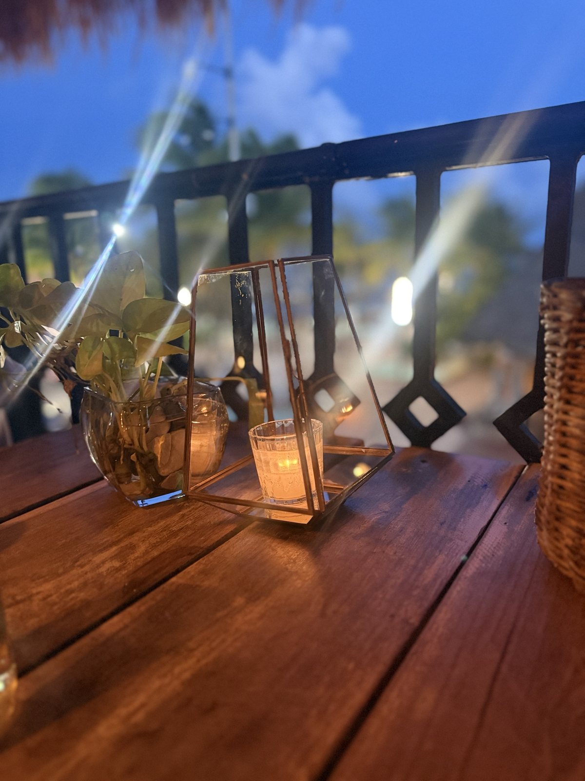A small glass and brass lantern holding a lit tea light on a rustic wood table at dusk