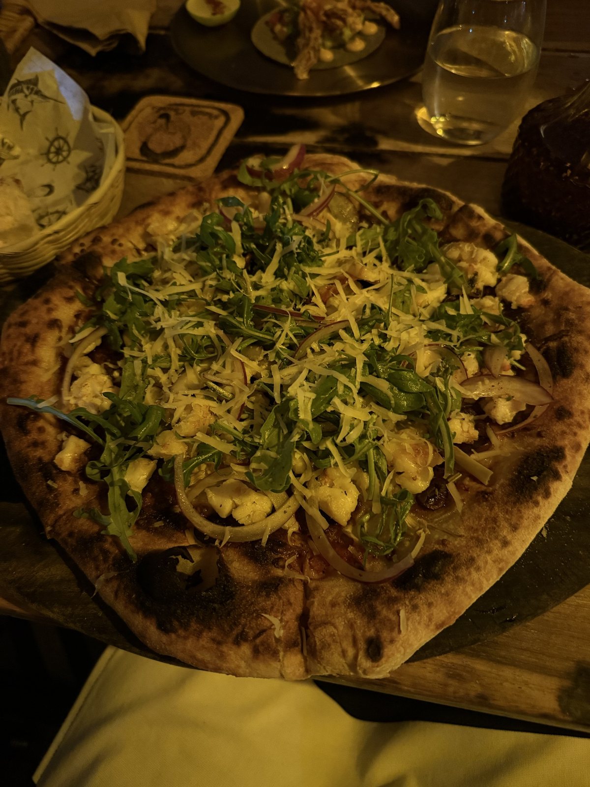 A wood-fired lobster pizza with arugula, shaved cheese and red onion on a wooden board